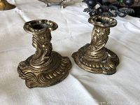 Pair of molded brass single candle holders with ornate scrolling pattern, showing detailed bases and candle sockets.