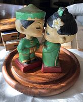 Photo of two vintage Chinese kissing dolls in traditional style attire on a wooden base, front and side view
