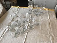 Full set of stemware items arranged on white and yellow tablecloth showing sherbet glasses, cordial glasses, and wine glasses.{","reason":"Shows all items in lot together and relative sizes."