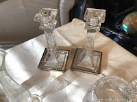Pair of clear cut glass candlestick holders with decorative brass bases, one with chip visible at the top.