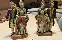 Front view of two painted porcelain colonial dancing couple figurines showing detailed costumes and facial features.