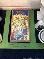 Framed tile artwork with Persian scene placed on floor against a wall, showing detailed colorful figures and landscape.