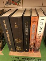 Photo showing 5 hardback fiction books standing upright, titles and authors visible on spines