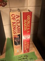 Image showing two hardback books by George R R Martin: 'A Clash of Kings' and 'A Feast for Crows' with dust jackets, standing upright on a wooden surface.