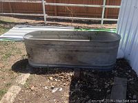 Full view of galvanized stock tank placed outdoors on ground with some dirt and leaves inside and outside