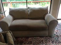 Front view of beige Rowe love seat with two cushioned seats and wide arms sitting on patterned rug near sliding glass door.