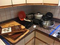 Overview of kitchen countertop showing induction cooktop, wooden cutting boards, colander, salad spinner, some stainless steel bowls and pans, and electric knife.
