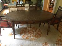 Full view of the oval walnut finish dining table surrounded by chairs.