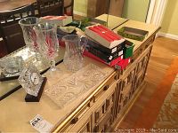 Wide angle photo of the mantel clock, crystal pitcher, crystal tray, boxes of candles on a wooden cabinet surface under a mirror