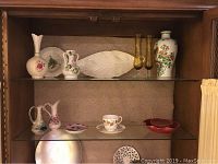 Cabinet shelf with Lenox gilt trim rose vase, leaf-shaped dish, Wedgwood cup and saucer, N.V. Koninklijke small plates and bowl, and Mikasa Christmas plate.