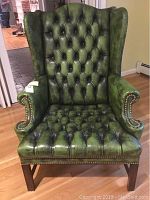 Front view showing deep tufted seat and back, green leather-like polyvinyl upholstery, wooden legs, and metal nailhead trim along armrests.