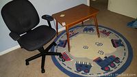 Wood table, Pottery Barn round train-themed rug, black office chair shown together in room.