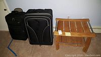Photo showing two black wheeled suitcases side by side and a wooden side table with slatted design.