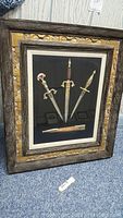 Full view of the shadowbox frame containing the three souvenir daggers and one sheath against a black backing.