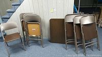 Overview of the folding chairs arranged in groups next to the folded table tops on the floor with a carpeted basement background.