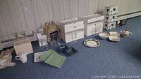 Wide view of assorted plates, stemware boxes, ceramic corn servers, and loose dishes on carpet.