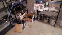 Wide shot of basement shelves with multiple kitchen appliances and cookware including juicer, pots, slow cooker, and pizza pans.