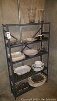 Full shelving unit with assortment of serving and decorative items mostly ceramics and glassware