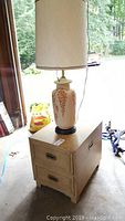 Ceramic lamp atop wooden two-drawer nightstand in garage, showing lamp design and nightstand drawers