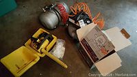 Two air compressors and yellow Sears Craftsman chainsaw in case shown on concrete floor with orange coiled hose attached to one compressor.