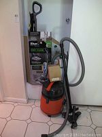 Photo showing the Shark Sonic Duo Pro floor scrubber with original packaging and the orange Fein wet dry vacuum with hose and wheels