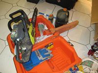 Ryobi 14-inch gas powered chainsaw with orange Husqvarna plastic carrying case, blue and gray gloves, oil bottles and tool inside the case.