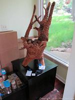 Full view of carved teak wood stump on black stand near window