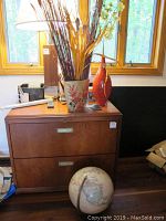 Lamp, decorative baskets, two vases on a wooden cabinet with natural light from window