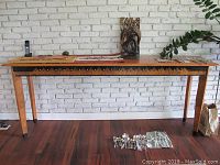 Full front view of wood sofa table against white brick wall with accessories on top and floor