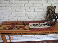 Wood carved wall art, fish design with red and black accents, small table runner with fish design, and two carved figures on a wooden table.