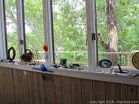 Four colored glass ball wind chimes displayed on a window ledge along with other decorative items including wire sculptures and small tiles.