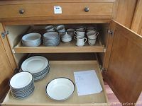 Kitchen cabinet with stacks of plates, cups and serving items inside.