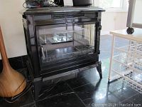 Black electric fireplace model SP5465 viewed from front left showing glass door and metal body on black marble floor.