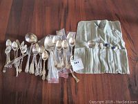 Overall assortment of sterling flatware laid out on wooden surface, including loose spoons, forks, and fabric roll.