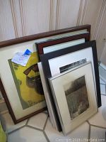 Six framed pieces of wall art stacked against wall showing various sizes and frame styles.