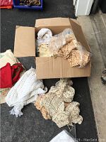 Box of various crocheted linens, doilies spilling from a cardio box, predominantly white and cream colored
