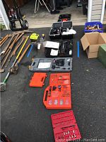 View of assorted hand tools, cases of drill and driver bits, power tools and accessories arranged on asphalt.