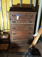 Front view of tall vintage wooden dresser with five drawers and metal handles, showing wear to finish.