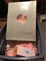 Closed Quiltex box shown with logo and image of mother kissing baby on the cover, atop plastic bin containing baby clothes and boxed shoes.