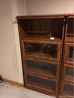 Full view of the barrister bookshelf showing three stacked glass cabinet doors with brass knobs and an open shelf on top.