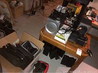 Overview of Bose speaker, Altec Lansing speakers, other electronic components and black bags on and around wooden table