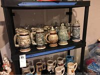 Photo of eight Avon beer steins with lids on two shelves. Varied designs and colors visible.