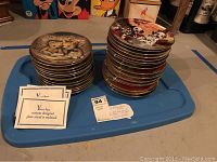 Two stacks of collector plates with visible illustrations of Dalmatians, cats, dogs, and bears on top. Accompanying cards for free custom plate stand included.
