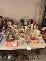 Overview of table with various perfume bottles, Goebel glass angels, ceramic animal figurines including bears, a glass domed music box, and assorted other collectible figurines.
