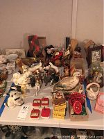Wide view of table with assorted figurines including dogs, ducks, music boxes, dolls, gold elephant figurine, and other decorative pieces.