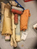 Wide view of two vintage Hungarian patterned paint rollers alongside several rolled canvases and painted cloths on the floor.