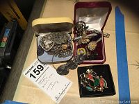 Photo showing multiple boxes of vintage jewelry including silver marcasite pieces, pins, brooches and a scarab style decorative item with a MaxSold tag describing items as marcasite, scarab, mosaic, and jewelry.