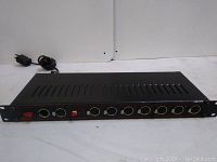 Front wide view of the black metal DMX booster showing multiple XLR inputs/outputs, red power button, and ventilation slots.