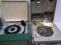 Two vintage portable turntables side by side, one with green felt case and internal speaker, the other with white base and integrated speaker under lid.