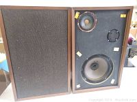 Front view of vintage wooden speaker, grille removed, showing 3 speaker drivers and visible damage on speaker surrounds and cabinet edges
